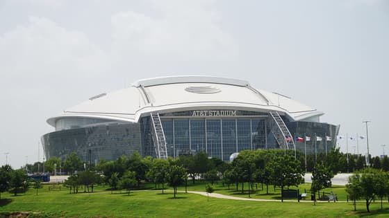 Vista exterior del AT&T Stadium en Arlington, Texas, con su techo blanco, la fachada de cristal y el parque verde que rodea la casa de los Dallas Cowboys.