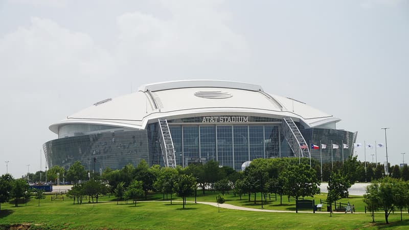 Vista exterior del AT&T Stadium en Arlington, Texas, con su techo blanco, la fachada de cristal y el parque verde que rodea la casa de los Dallas Cowboys.