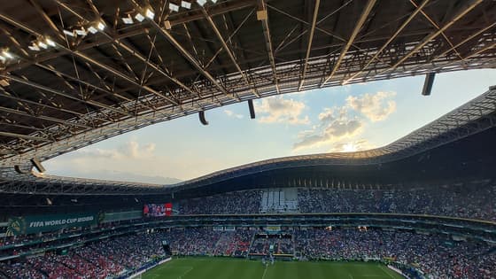 Interior del Estadio BBVA de Monterrey al atardecer, con las gradas llenas, la cancha iluminada y el techo ondulado visto desde la parte alta.