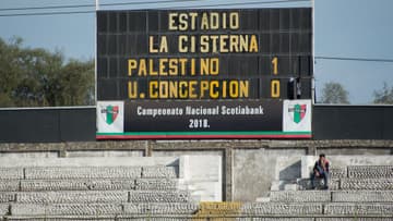 Tablero marcador de un estadio de futbol con letras amarillas y el resultado 1-0 sobre las gradas de concreto casi vacías