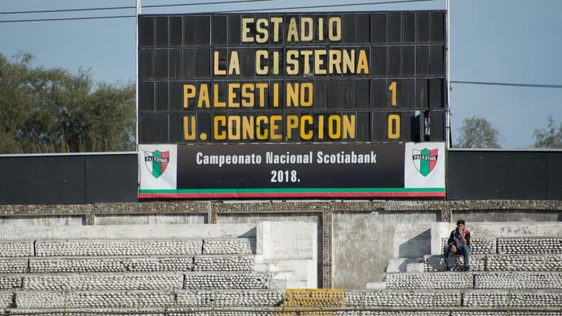 Tablero marcador de un estadio de futbol con letras amarillas y el resultado 1-0 sobre las gradas de concreto casi vacías