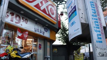 Fachada de una tienda OXXO en la Ciudad de México, vista en contrapicado: rótulo OXXO, entrada de la tienda, lonas de promoción (agua e-pura, $19