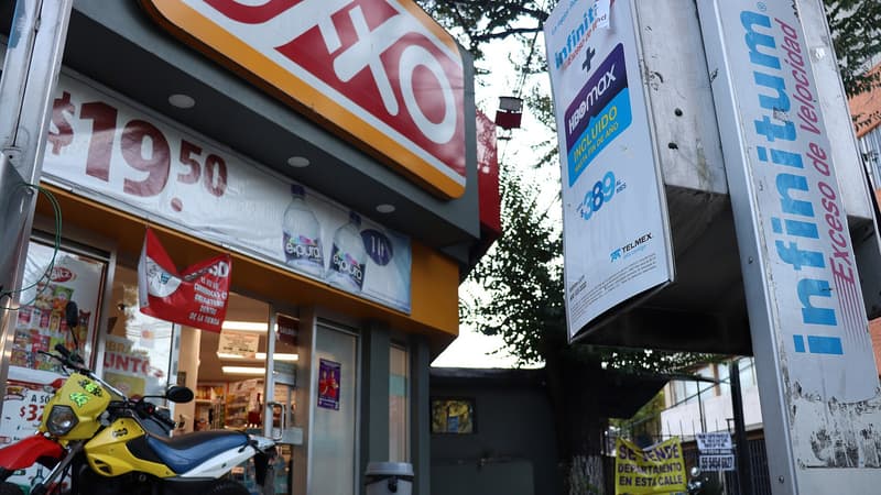 Fachada de una tienda OXXO en la Ciudad de México, vista en contrapicado: rótulo OXXO, entrada de la tienda, lonas de promoción (agua e-pura, $19