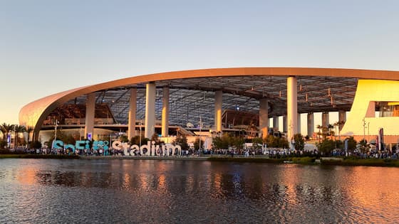 Exterior del SoFi Stadium en Inglewood, California, al atardecer, con aficionados caminando junto al letrero del estadio en un día de partido de la NFL.